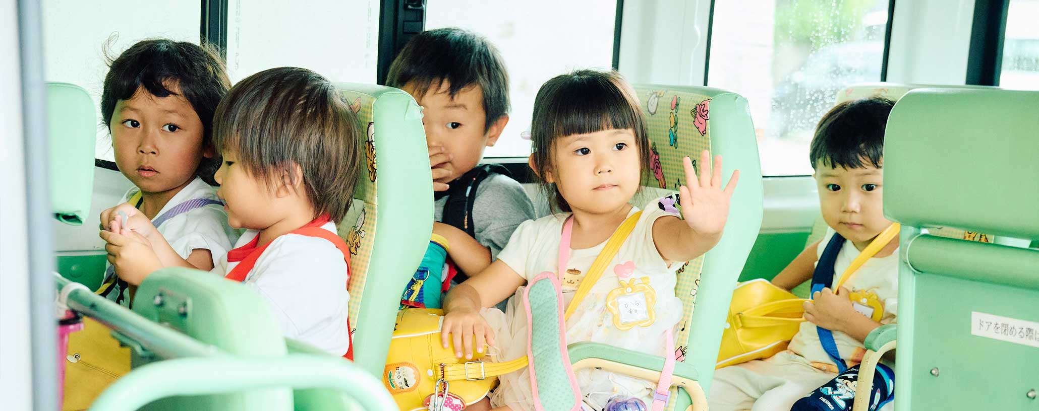 スクールバスに乗り込む子どもたちと、乗車を確認する職員